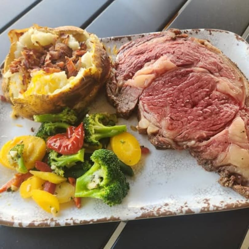 Prime rib with a loaded baked potato and mixed vegetables on a rustic plate.