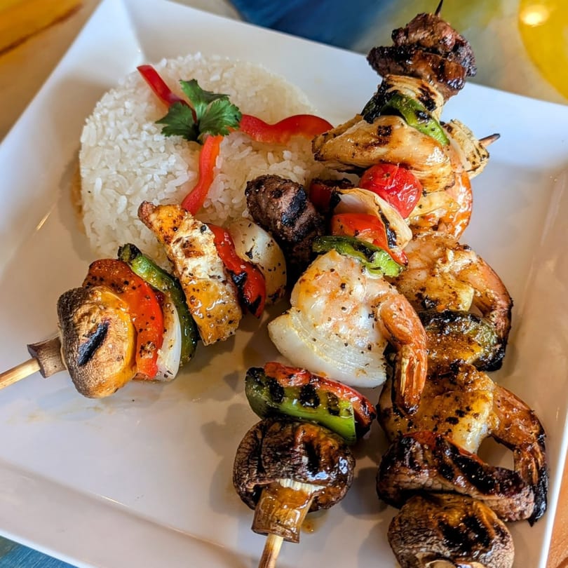 Grilled shrimp, chicken, and beef skewers with vegetables and a side of white rice.