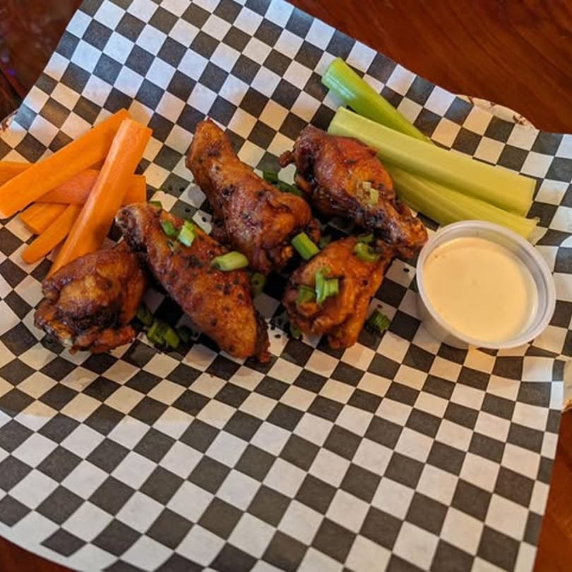 Cold Springs Crossing Bar & Grill's chicken wings with carrots, celery, and dipping sauce on checkered paper.