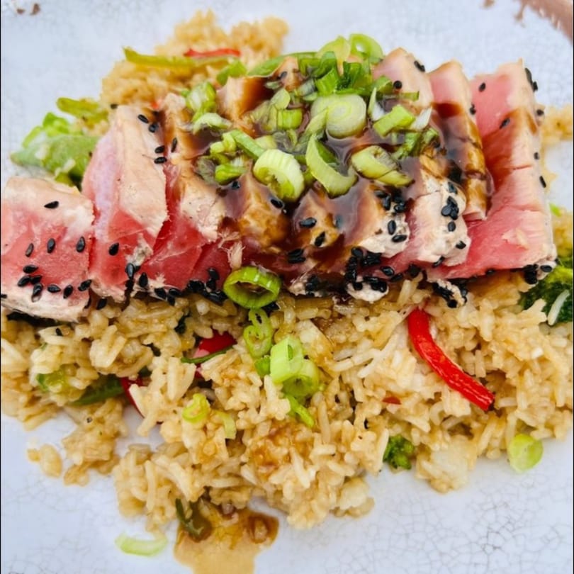 Seared tuna with black sesame seeds, green onions, and sauce, served over fried rice.
