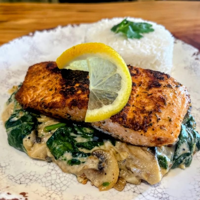 Grilled salmon with lemon, creamy spinach, mushrooms, and a side of white rice.