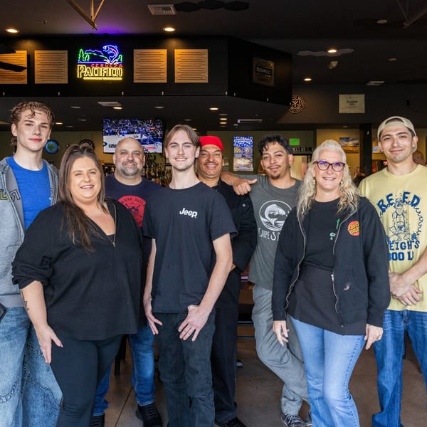 Nine smiling staff members, including men and women, pose together inside Cold Springs Crossing Bar & Grill.