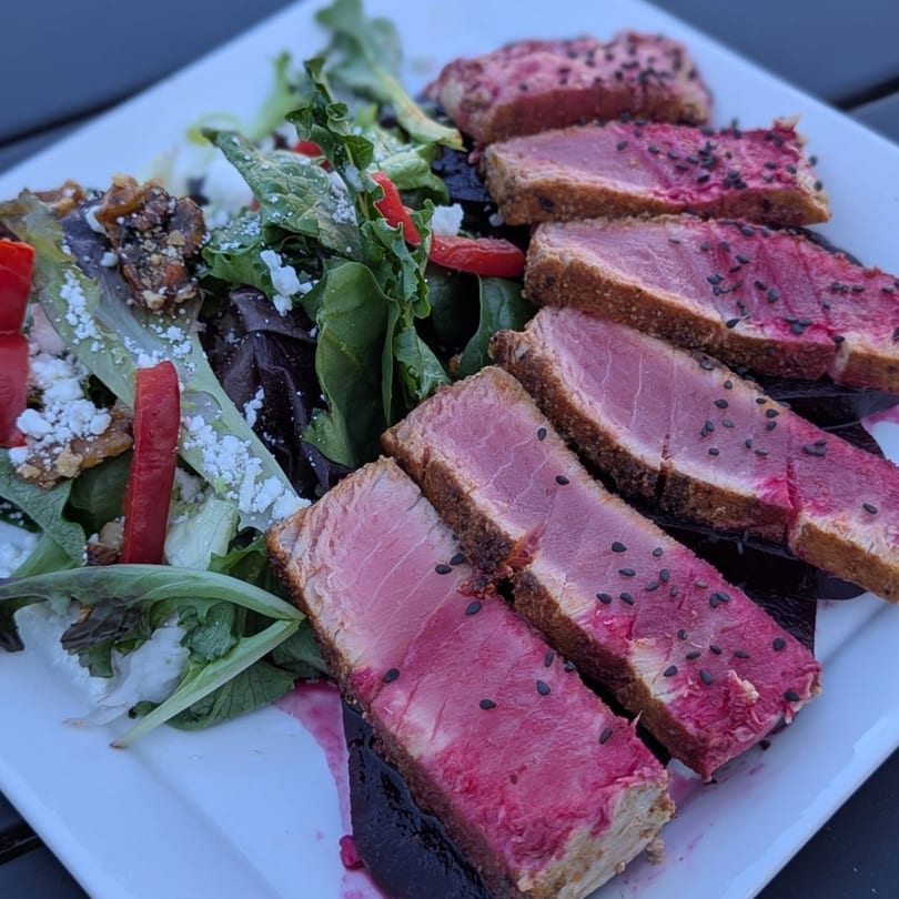 Seared tuna slices with black sesame seeds, served alongside a fresh green salad with feta and nuts.